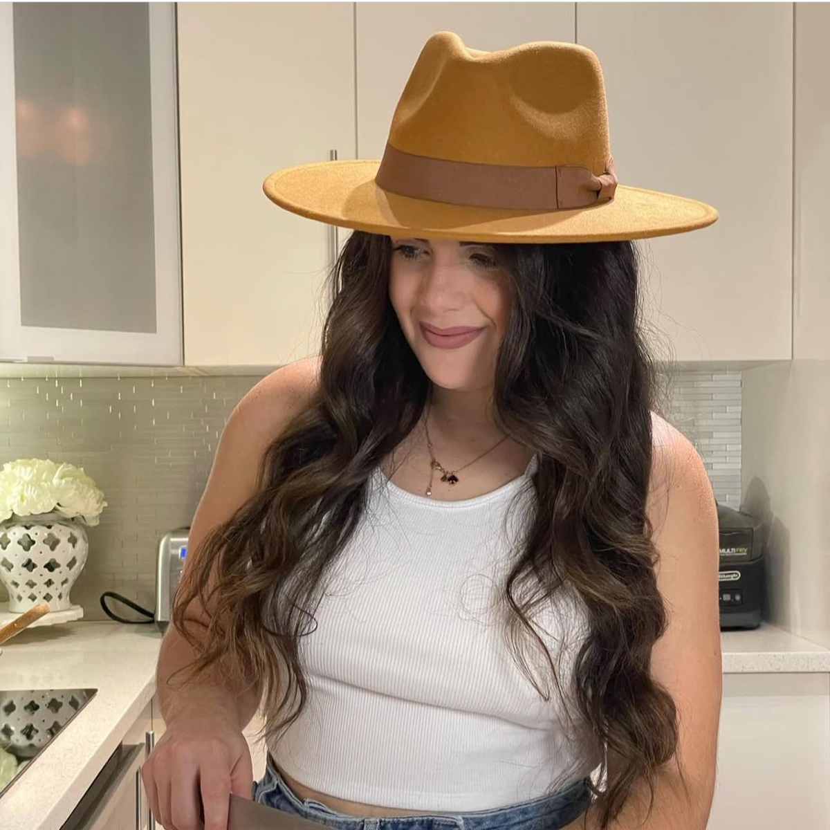 Woman wearing a tan Dion wide-brim fedora while preparing food in a kitchen.