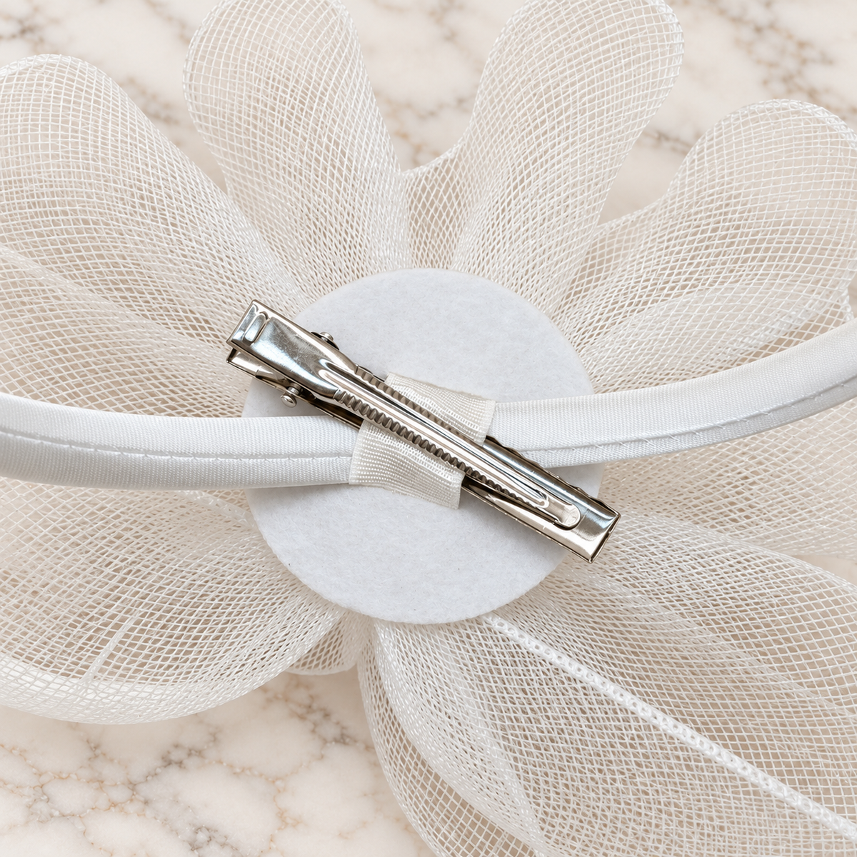Underside of white Anastacia fascinator showing headband and hair clip on light marble