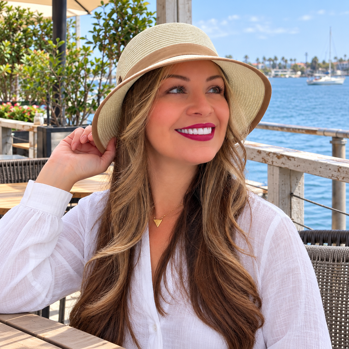 Model wearing Catalina White bucket hat with beige trim at a waterfront cafe, square image.