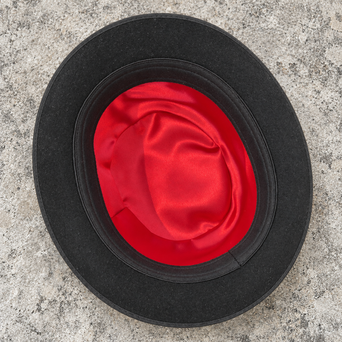 Interior of Chaplin black wool derby hat with red lining and fixed inner band on a gray stone background