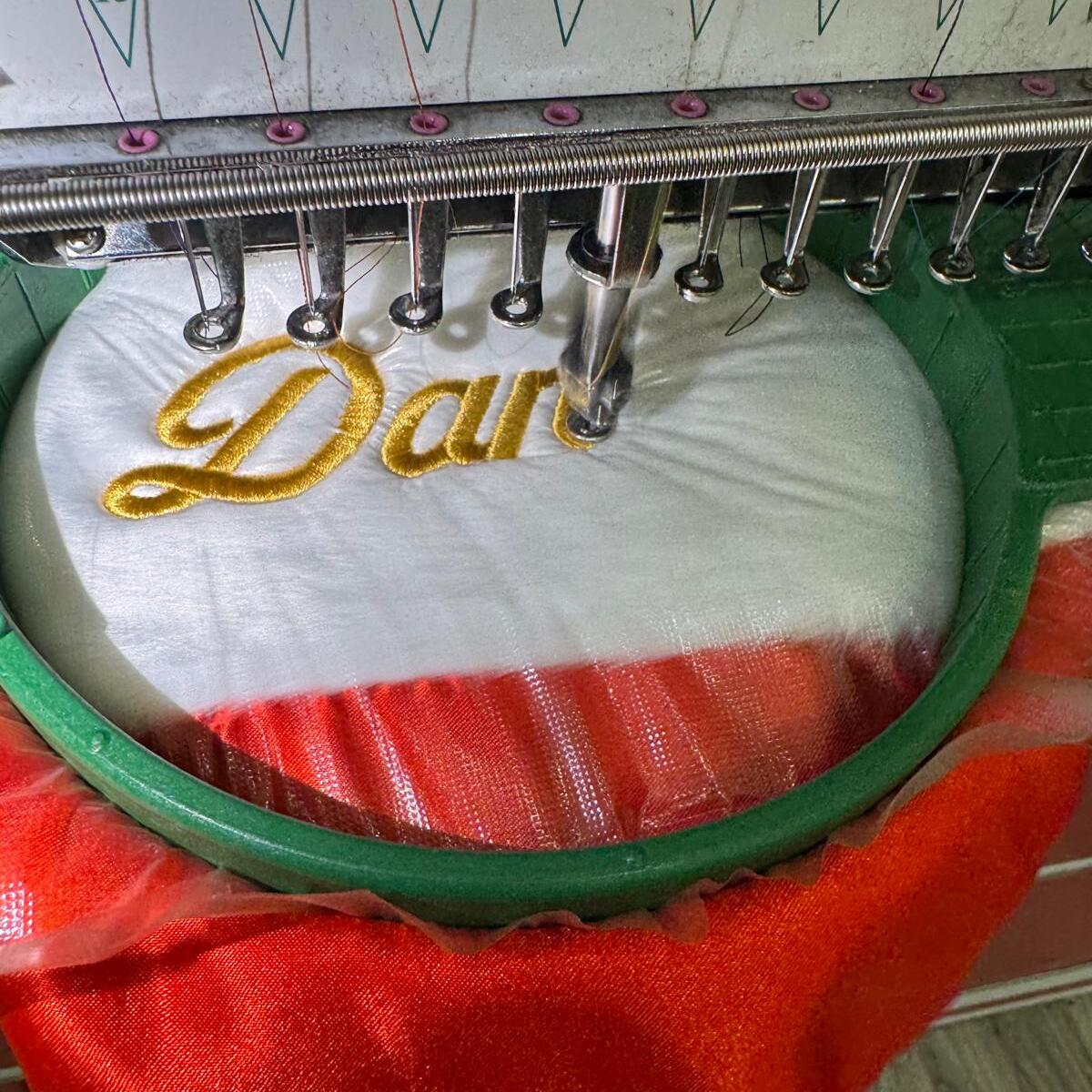 Gold name embroidery in progress on a Santa hat