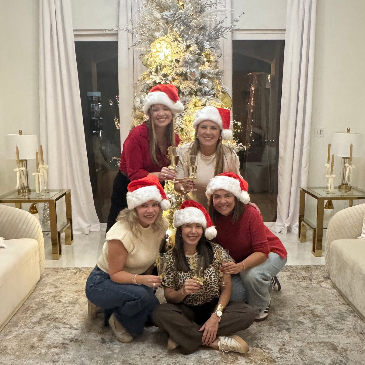 Five friends wearing Santa hats under a Christmas tree