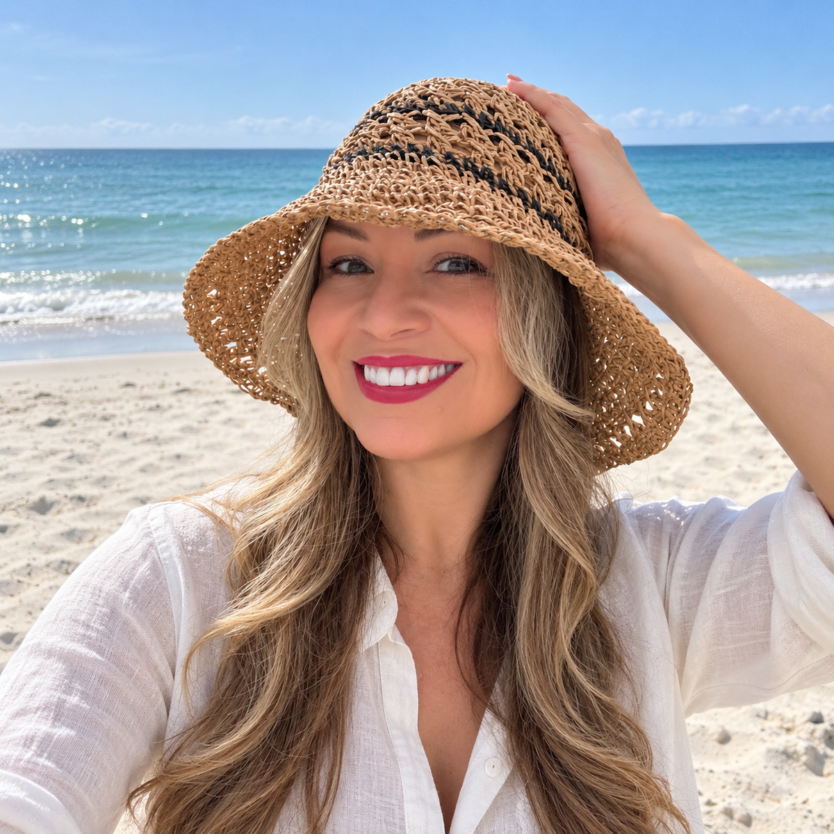 Woman in linen shirt wearing Karina tan crochet bucket hat with dark stripes on a sandy beach
