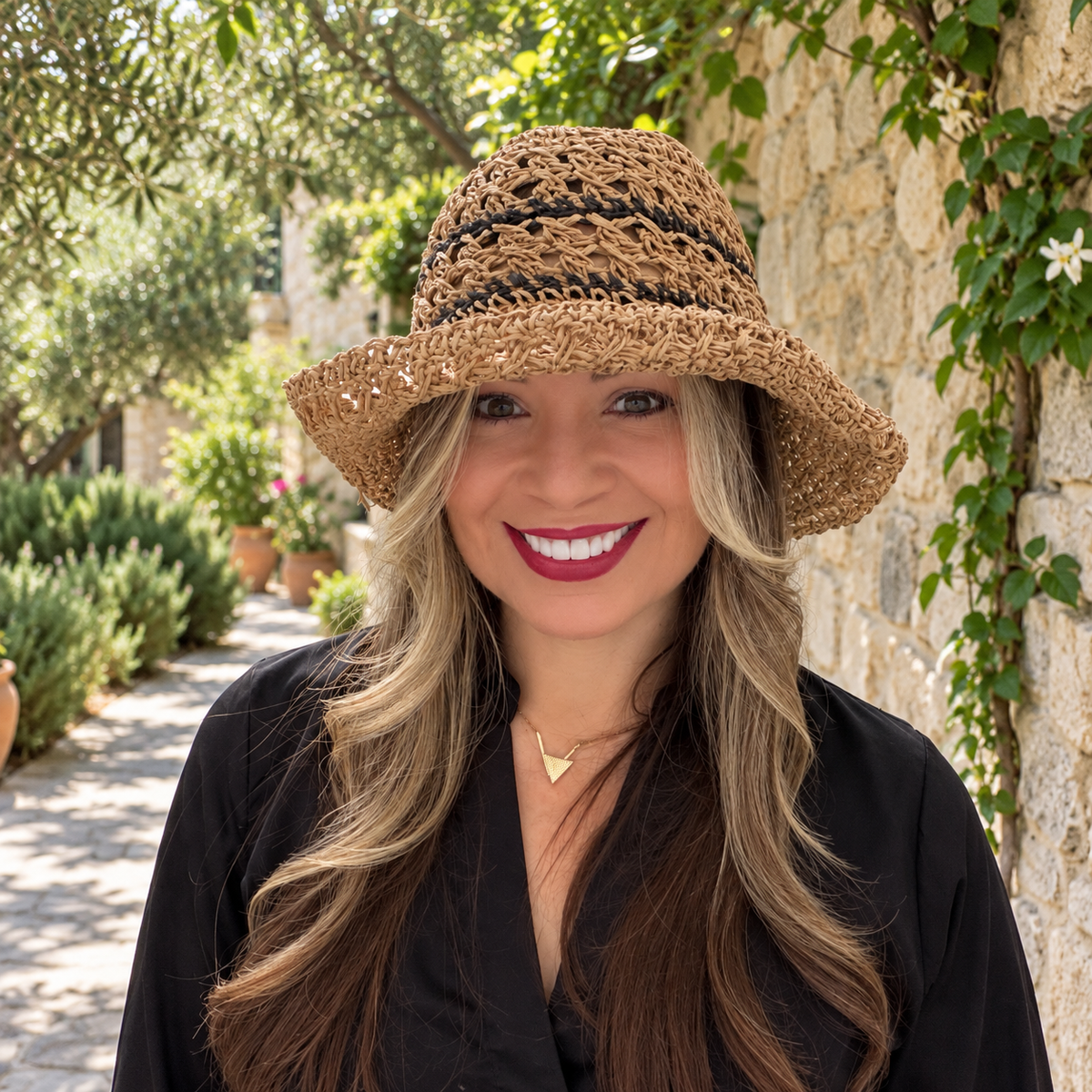 Woman wearing Karina tan crochet bucket hat with dark woven stripes in a stone garden
