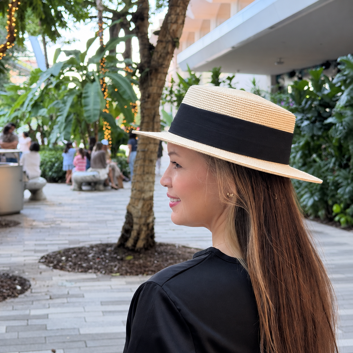 Woman wearing Lola Beige boater hat in a real outdoor courtyard, side profile