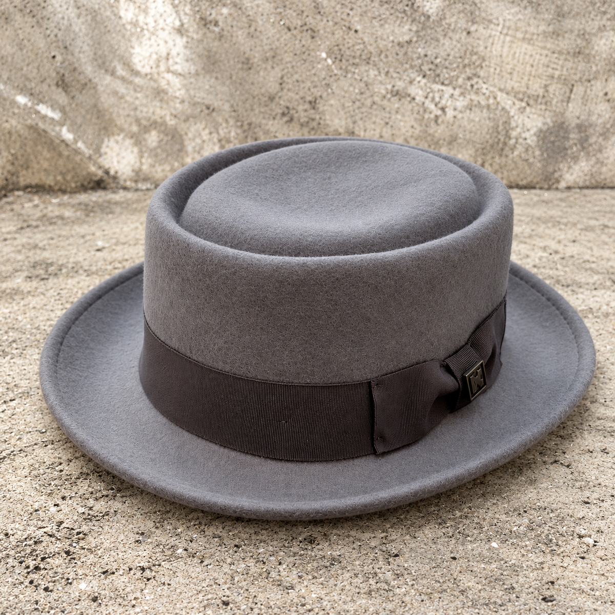 Monte Carlo gray wool hat showing ribbon bow and decorative pin on a textured stone background