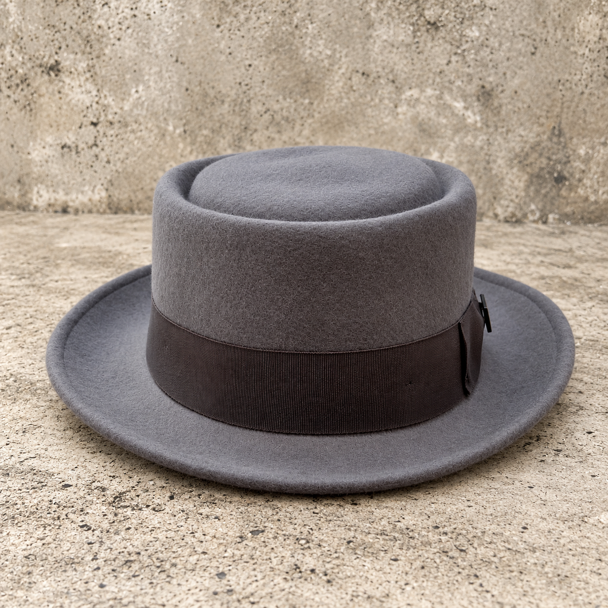 Angled side view of Monte Carlo gray wool hat with dark ribbon band on a textured stone background
