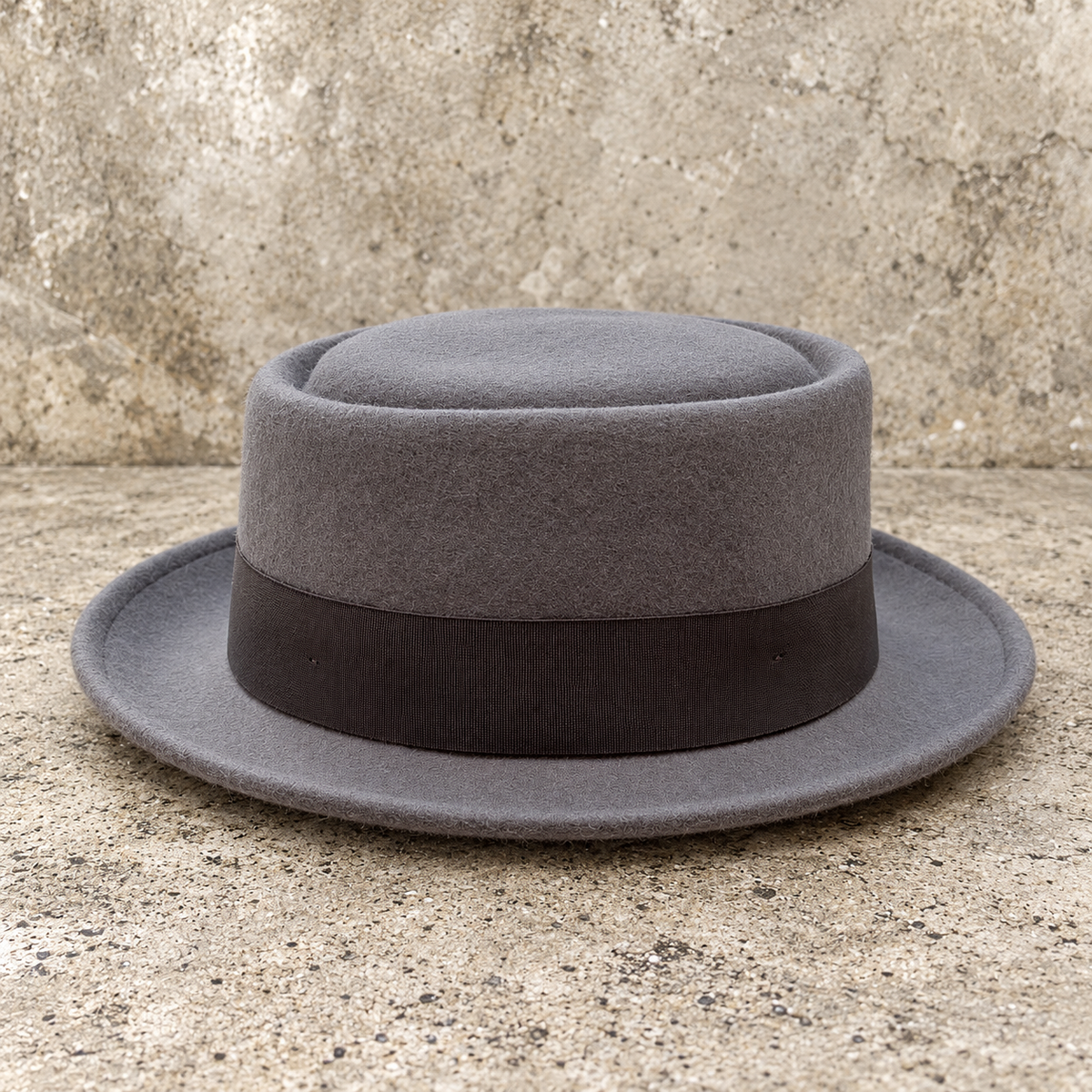 Monte Carlo gray wool hat showing its recessed crown and gently upturned brim on a textured stone background