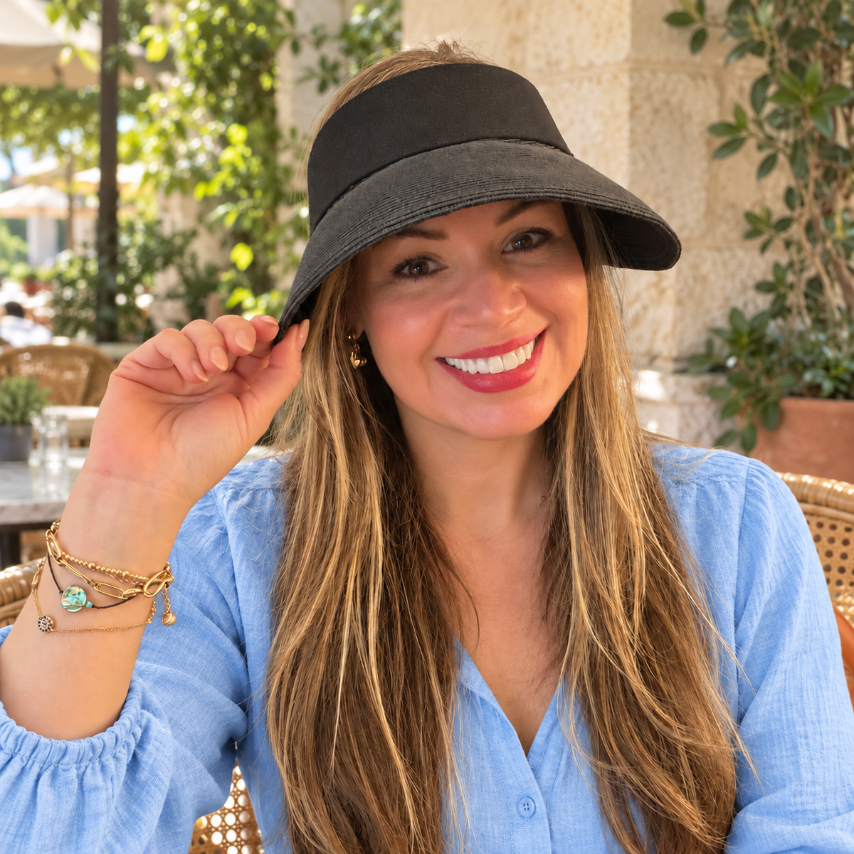 Woman wearing the Nala Black sun visor with a light blue blouse at an outdoor cafe