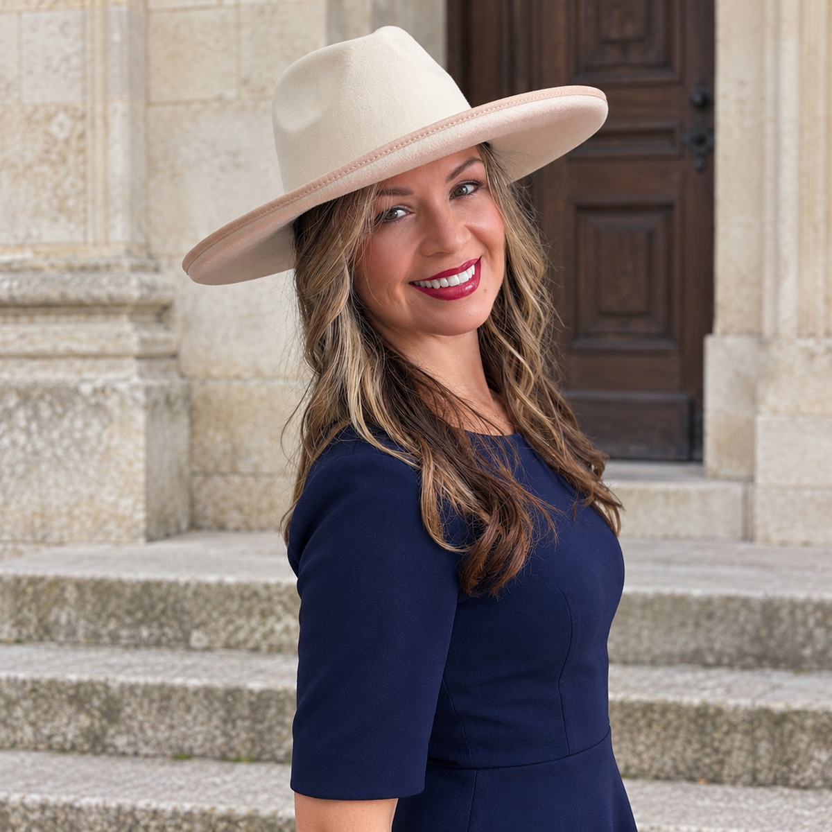 Woman wearing the light Orfeo vegan felt wide brim fedora with a navy dress outside a classic stone entrance.