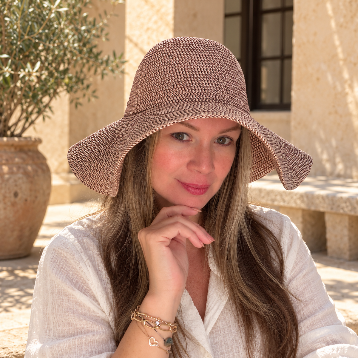 Woman wearing Paola grape tweed floppy brim sun hat in a sunlit courtyard