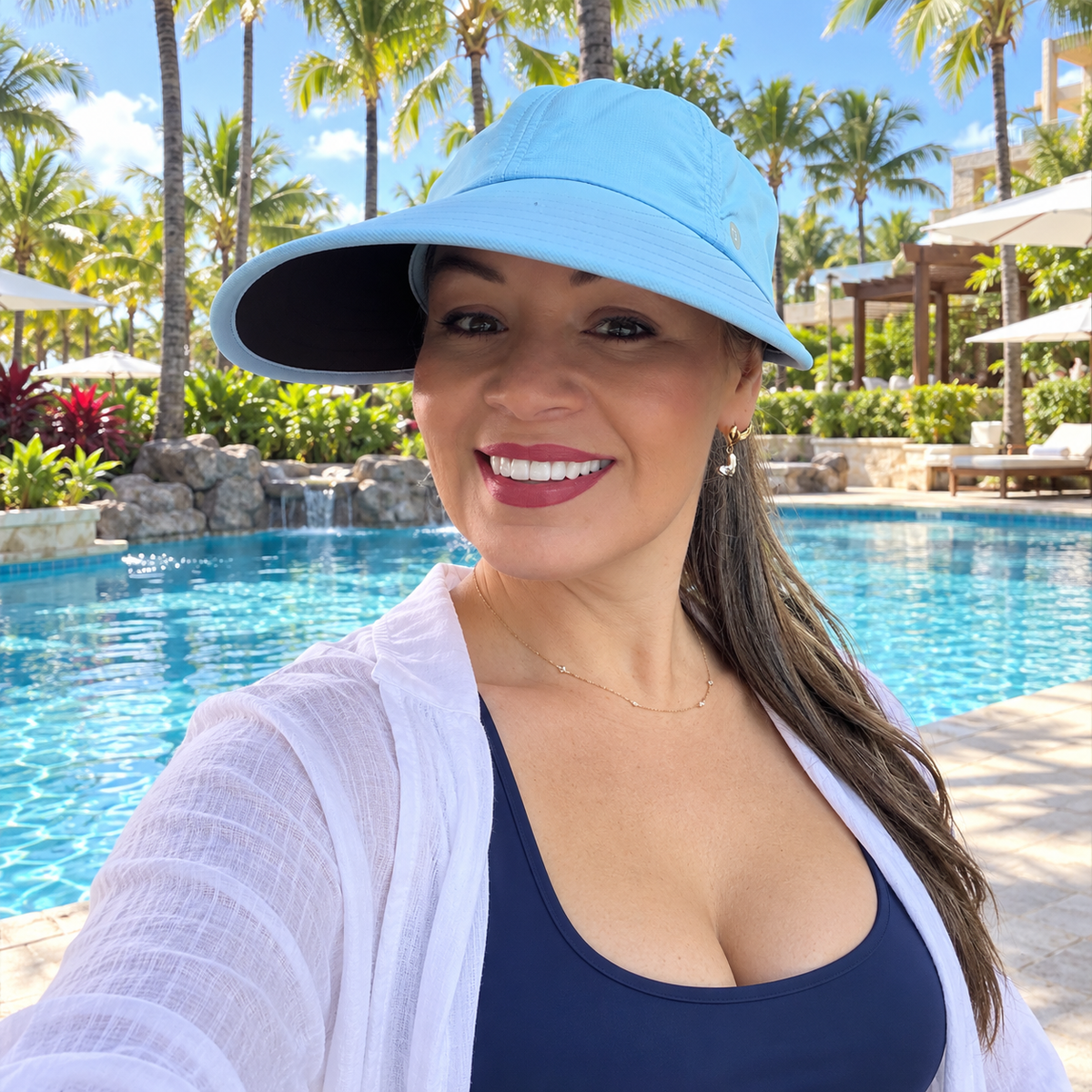 Woman wearing the blue Pia ponytail visor hat beside a resort pool.