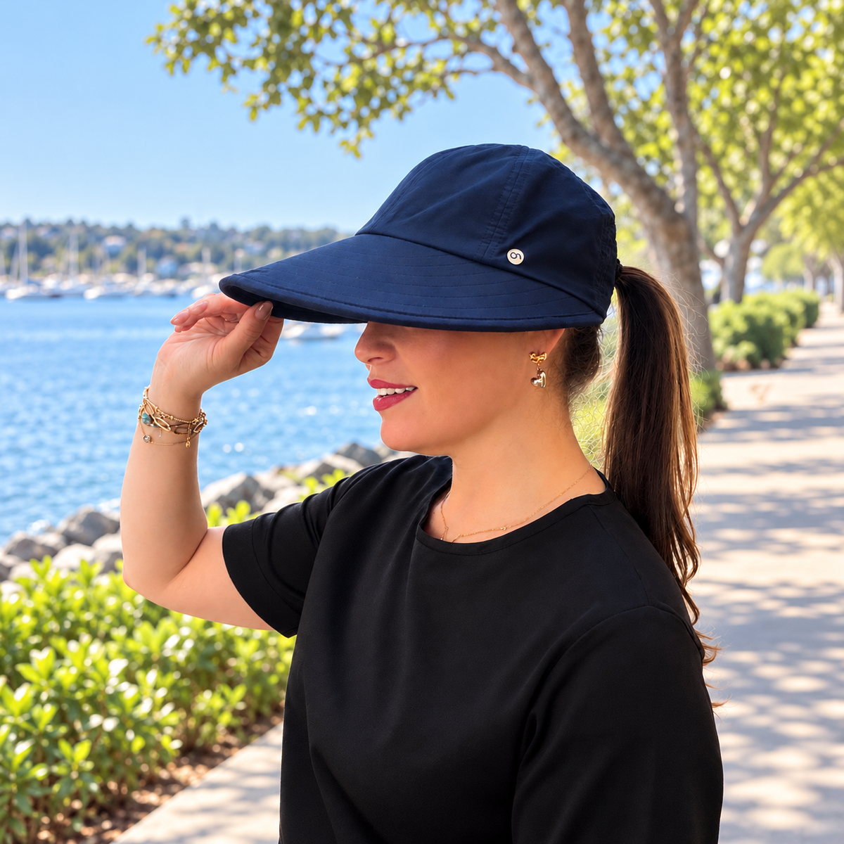 Side view of the navy blue Pia visor hat with a ponytail beside a waterfront path.