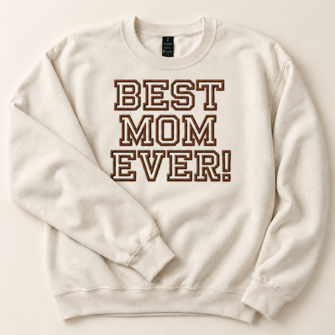 Cream sweatshirt with large centered brown BEST MOM EVER! embroidery on an ivory studio background