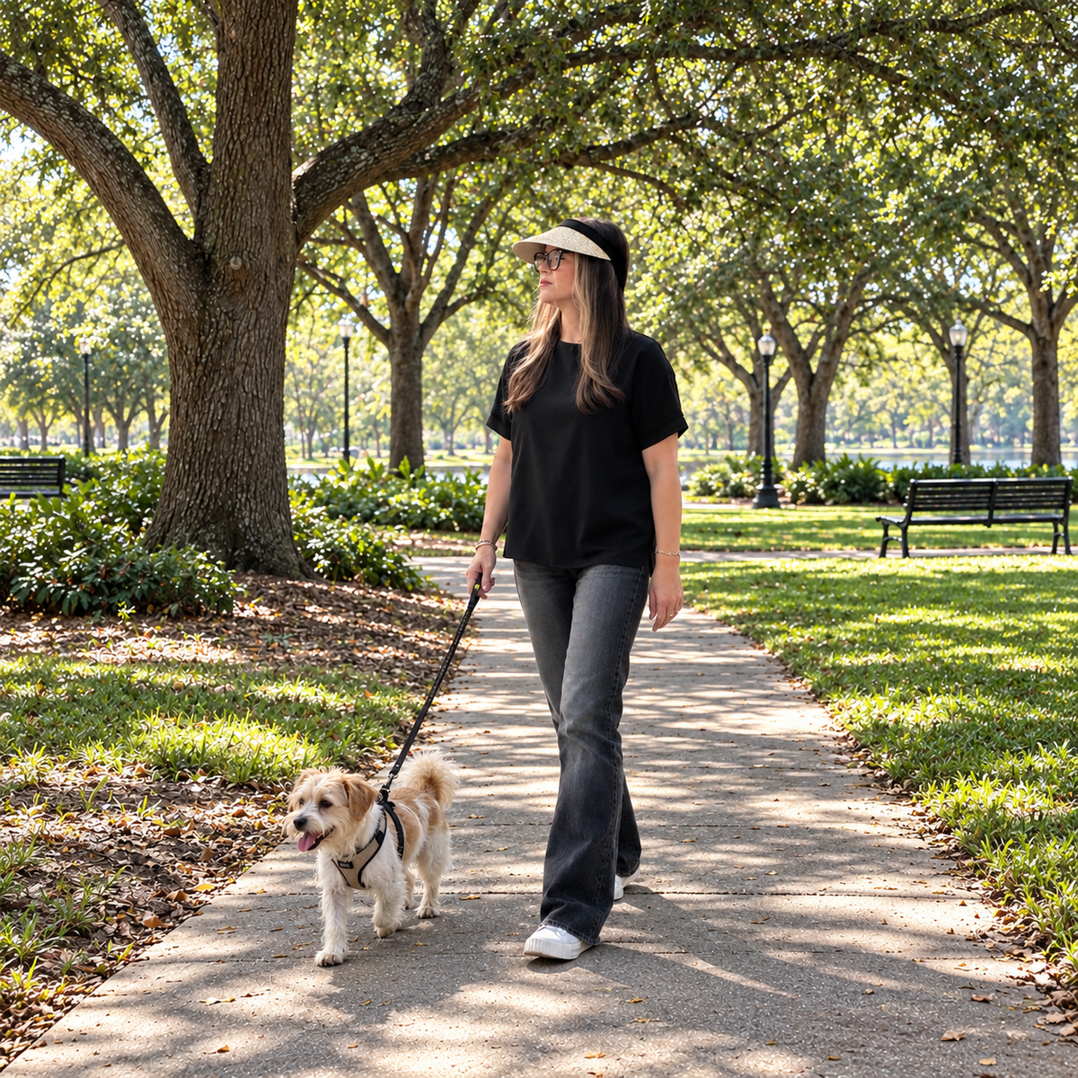 Woman wearing the Valeria woven clip-on sun visor with a black band while walking a small dog in a leafy park.