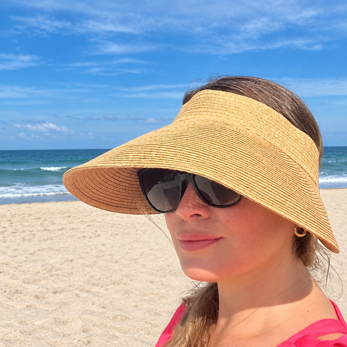 Woman wearing the natural Zara extra-wide brim sun visor and sunglasses at the beach.