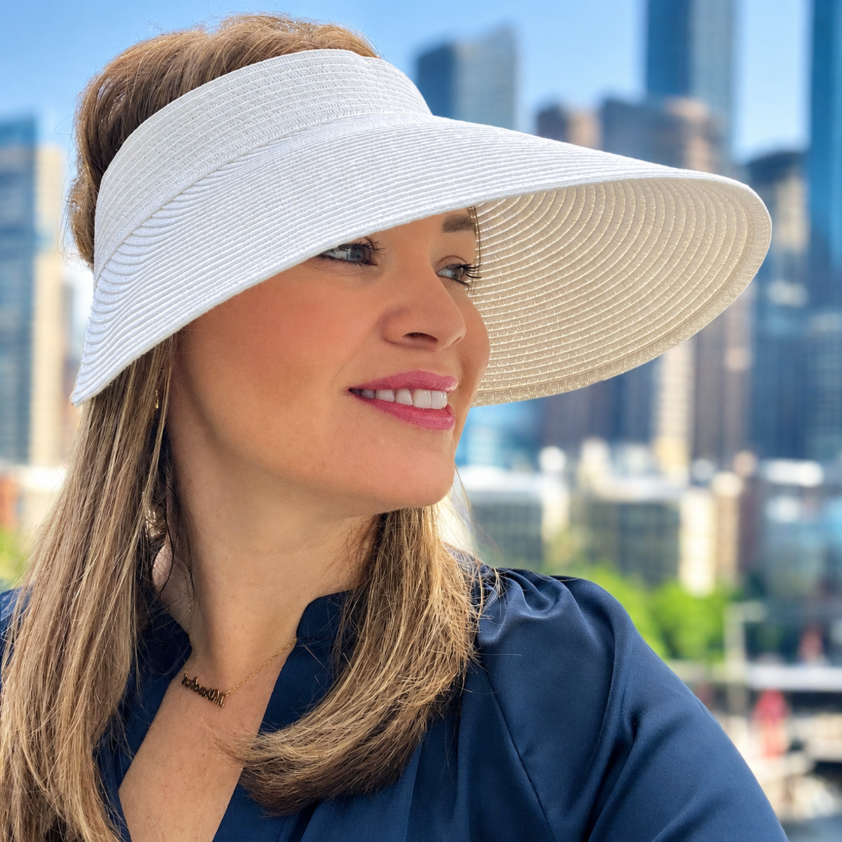 Woman wearing the white Zara extra-wide brim sun visor beside a waterfront skyline.